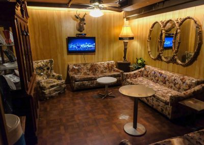 Wood-paneled vintage trailer interior with floral couches, table lamp and round mirror