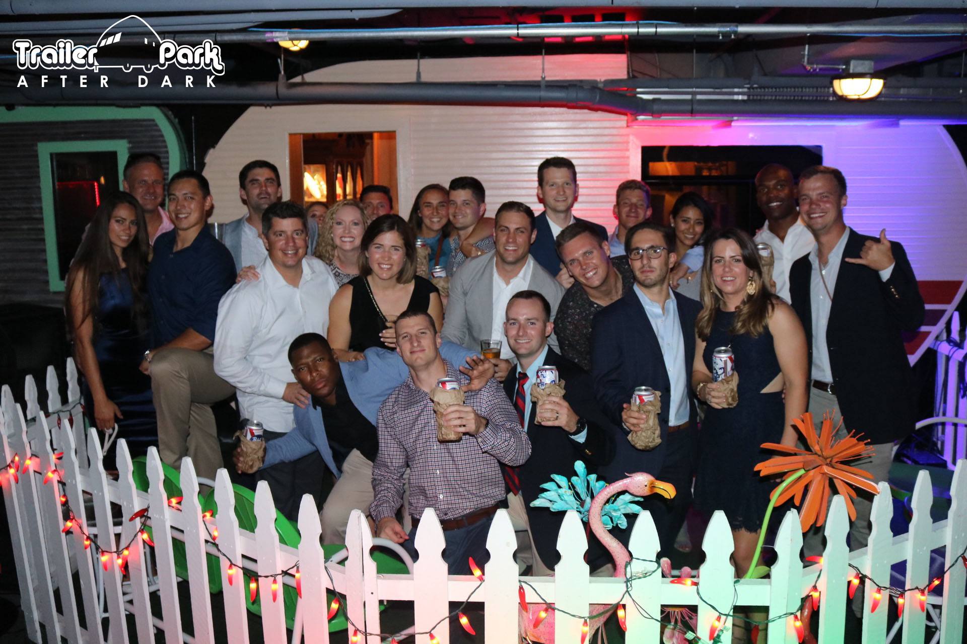 Large corporate holiday party group posing behind the white picket fence at Trailer Park After Dark in downtown San Diego