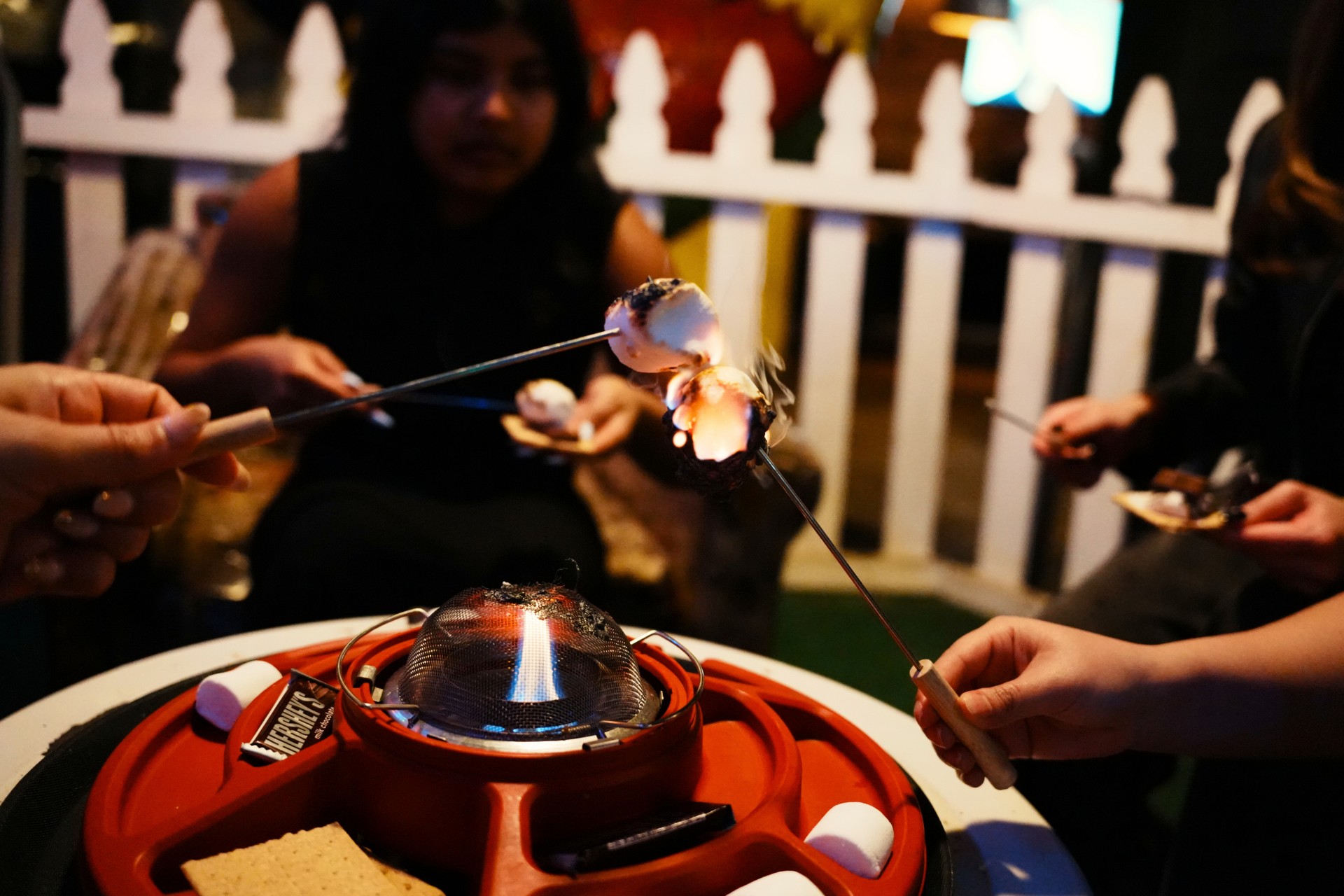 Guests roasting marshmallows over a tabletop s'mores fire pit during a group party at Trailer Park After Dark