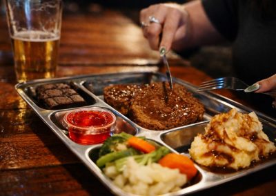 Diner cutting into meatloaf on a divided cafeteria tray with mashed potatoes