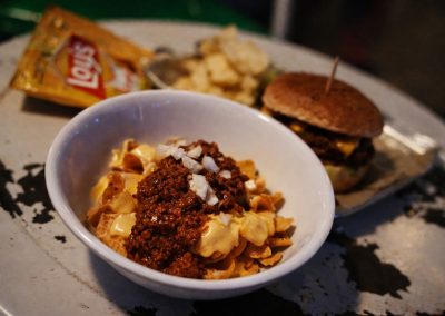 Chili cheese tots in a bowl beside a burger and a bag of Lay's chips