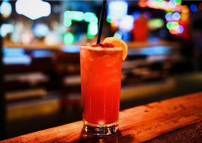 Tall red cocktail with an orange slice and straw on the bar