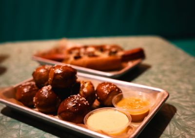 Soft pretzel bites with cheese and mustard dipping sauces beside a hot dog